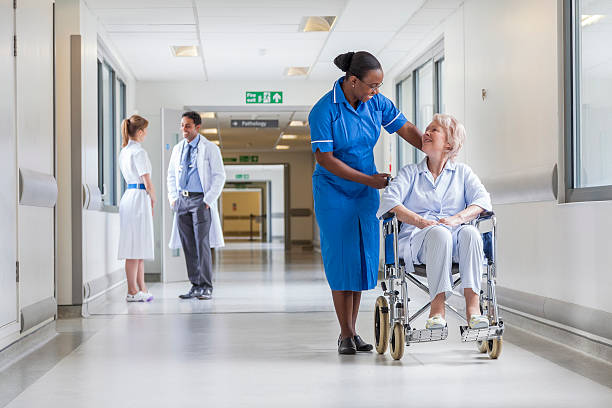 Senior female woman patient in wheelchair sitting in hospital corridor with African American female nurse doctor and nurse in background